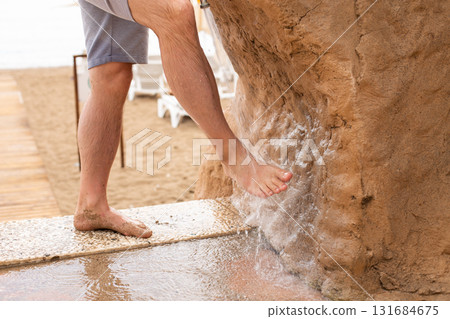 Man washing his feet with shower to clean them from the sand standing on the beach on the seashore. 131684675