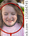 Girl holding badminton racket in front of face smiling with eyes closed 131684745