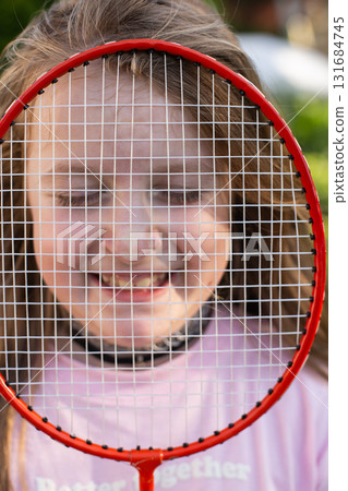 Girl holding badminton racket in front of face smiling with eyes closed 131684745