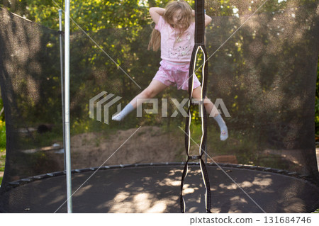 Child girl jumping on trampoline outdoors in the yard on summer vacation. 131684746