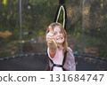 Happy excited child girl sitting on trampoline outdoor showing thumb up sign 131684747
