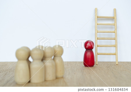 Red wooden figure standing before ladder with trusted followers representing ambition and leadership growth. 131684834