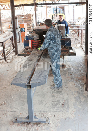Male worker saws log on machine. Woodworking company. Process of processing logs at sawmill. Sawing tree trunk. Sawmill. Male worker saws log on machine. Woodworking company. Process of processing logs at sawmill. Sawing tree trunk. Sawmill. 131684907