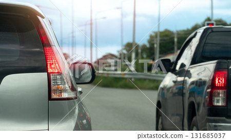 Rear side car stop and turn on brake light. Two car prepare starting from an intersection or race. Traffic jam on the road with cars on the side. blurred background of grass and pole light. Rear side car stop and turn on brake light. Two car prepare starting from an intersection or race. Traffic jam on the road with cars on the side. blurred background of grass and pole light. 131685037
