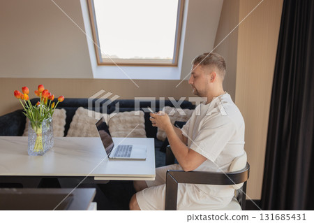 Man using smartphone while working with laptop at home office. Concept of remote work, online communication, fintech, digital banking, e-commerce, productivity and technology Man using smartphone while working with laptop at home office. Concept of remote work, online communication, fintech, digital banking, e-commerce, productivity and technology 131685431