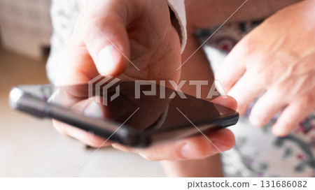 A man holds a smartphone in his hands. The phone has a sleek design and a dark screen. The background is blurred, focusing on the phone and hands. 131686082