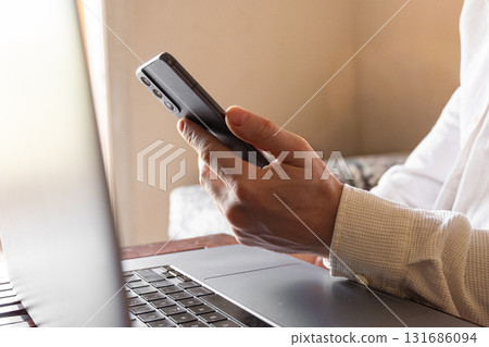 A man holds a smartphone in his hands. The phone has a sleek design and a dark screen. The background is blurred, focusing on the phone and hands. A man holds a smartphone in his hands. The phone has a sleek design and a dark screen. The background is blurred, focusing on the phone and hands. 131686094