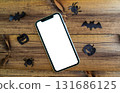 Mockup, smartphone, paper black bat, spiders and pumpkins on wooden background. Halloween background. 131686125