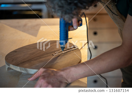 Man sealing cracks on finished wooden item with hot silicone to prepare for epoxy resin filling 131687154