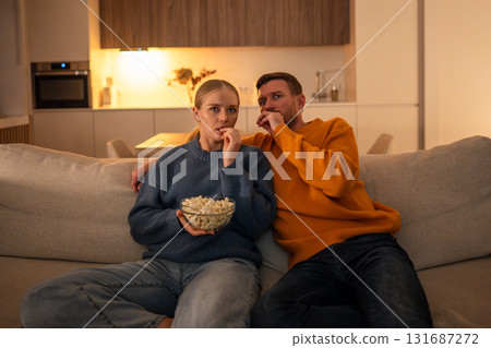 Fearful shocked couple watch thriller movie with popcorn at home. Family scared movie night Fearful shocked couple watch thriller movie with popcorn at home. Family scared movie night 131687272