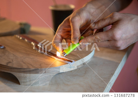 Carpenter hands removing air bubbles from liquid epoxy resin in wood crack using lighter flame 131687278