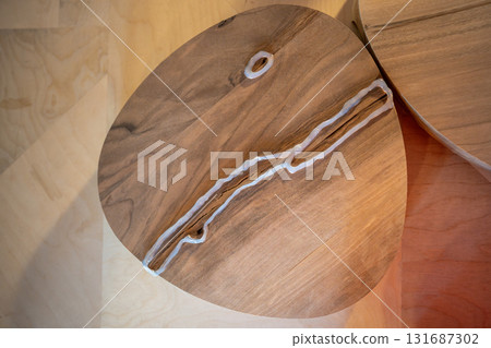 Sealing cracks on finished wooden surface with hot silicone to prepare for epoxy resin fill 131687302