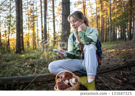 Pleased woman with phone sharing mushroom photo on social media rest in forest, satisfied forager 131687325