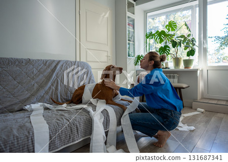 Torn toilet paper everywhere as dog gets gentle scolding from female owner, playful pet mischief Torn toilet paper everywhere as dog gets gentle scolding from female owner, playful pet mischief 131687341