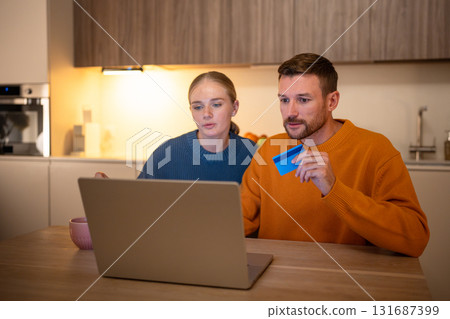 Thoughtful husband and wife planning trip on laptop at table using bank card for bookings payment Thoughtful husband and wife planning trip on laptop at table using bank card for bookings payment 131687399