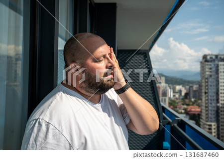 Fat man suffers dying from heat. Guy on balcony under hot summer sun sweats from high temperatures Fat man suffers dying from heat. Guy on balcony under hot summer sun sweats from high temperatures 131687460