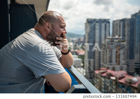 Overweight man suffering from heat in summer standing on balcony looking at street. Overweight man suffering from heat in summer standing on balcony looking at street. 131687494