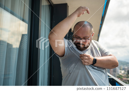 Overweight man suffering from heat, over sweating in summer standing on balcony in summer. 131687527
