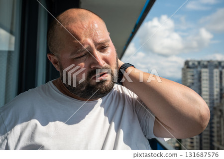 Bearded man in summer sun on balcony. Guy closed eyes in displeasure discomfort holding on to neck, Bearded man in summer sun on balcony. Guy closed eyes in displeasure discomfort holding on to neck, 131687576