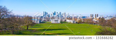 Beautiful green space of Greenwich Park features people enjoying the day, while modern buildings of London rise in the background against a clear blue sky. Beautiful green space of Greenwich Park features people enjoying the day, while modern buildings of London rise in the background against a clear blue sky. 131688282