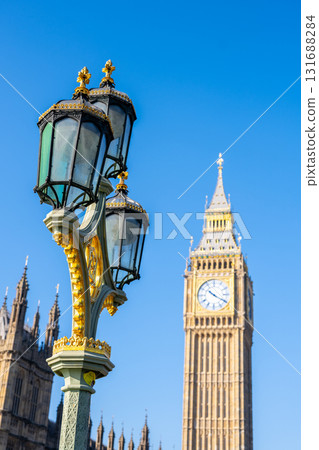 Big Ben stands majestically against a clear blue sky, while an ornate lamppost adorned with gold details highlights the vibrant architecture of London. Big Ben stands majestically against a clear blue sky, while an ornate lamppost adorned with gold details highlights the vibrant architecture of London. 131688284
