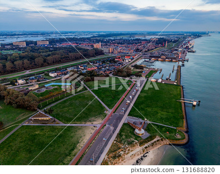 Aerial view of coastal town dense buildings, marina with docks, circular park structure, beach, and forested edges blend urban density with recreational and natural waterfront elements. Aerial view of coastal town dense buildings, marina with docks, circular park structure, beach, and forested edges blend urban density with recreational and natural waterfront elements. 131688820
