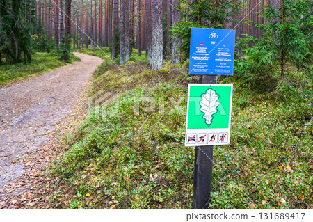 Forest trail with bicycle route and protected area signs showing oak leaf and restriction icons 131689417