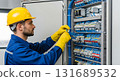 Man in hard hat and gloves working on electrical panel with blue wires and terminal blocks inside cabinet 131689532