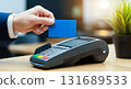 A person holding a blue credit card over a pos terminal for payment transaction in a store setting 131689533