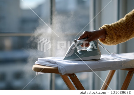 Steam iron applied to a shirt on an ironing board near a window in a bright room 131689688