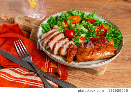 Delicious grilled duck breast served with fresh garden salad and cherry tomatoes at a rustic dining table 131689926
