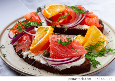 sandwich with freshly smoked salmon, on black bread, with cottage cheese, with herbs and red onions, capers and pieces of citrus fruits, on a marble countertop, breakfast, no people, 131689942