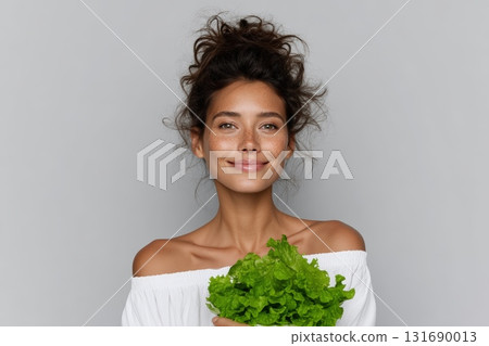 Woman smiling while holding fresh green lettuce in a studio setting Woman smiling while holding fresh green lettuce in a studio setting 131690013