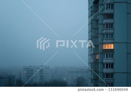 Fog envelops apartment buildings with a warm light glowing from a window at dusk 131690049