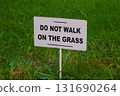 "Do not walk on the grass" sign mounted on a white rectangular board. The sign is set against a background of green grass. 131690264