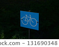 An informational sign indicating a bicycle lane. The sign is a blue rectangle with a white bicycle silhouette, set against a background of green foliage. 131690348