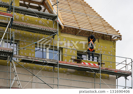 Worker on scaffolding insulating house facade with mineral wool during construction Worker on scaffolding insulating house facade with mineral wool during construction 131690406