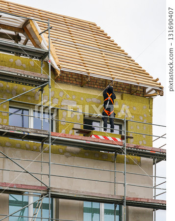 Worker on scaffolding insulating house facade with mineral wool during renovation works Worker on scaffolding insulating house facade with mineral wool during renovation works 131690407