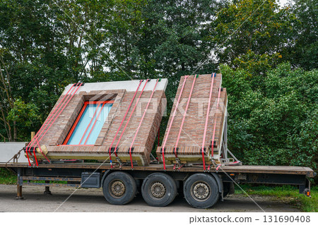 Prefabricated brick wall panels with windows transported on flatbed truck at construction site 131690408
