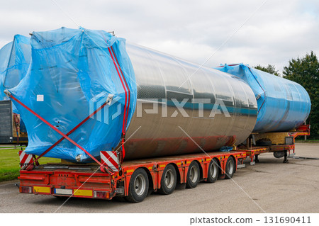 Large stainless steel industrial tanks on flatbed truck secured with blue covers for transport Large stainless steel industrial tanks on flatbed truck secured with blue covers for transport 131690411