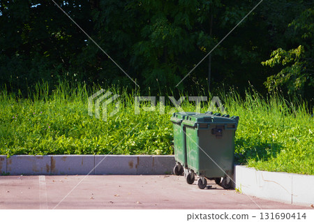 Green garbage bins on the street, placed on a paved area near the curb. Green garbage bins on the street, placed on a paved area near the curb. 131690414