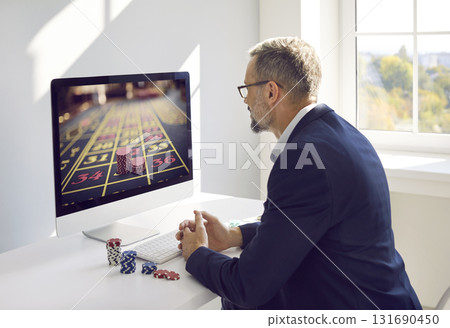 Concentrated businessman playing online casino while sitting at workplace in office. 131690450