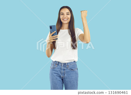 Portrait of happy young woman holding mobile phone, smiling and doing yes gesture Portrait of happy young woman holding mobile phone, smiling and doing yes gesture 131690461