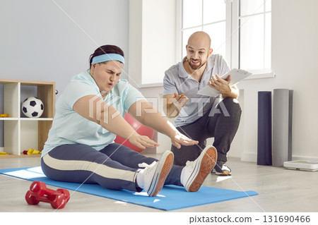 Overweight woman trying to do seated forward bend during sports workout with trainer Overweight woman trying to do seated forward bend during sports workout with trainer 131690466