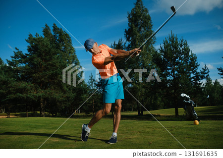 Swinging a golf club on a sunny day at a lush green course with a blue sky in the background Swinging a golf club on a sunny day at a lush green course with a blue sky in the background 131691635