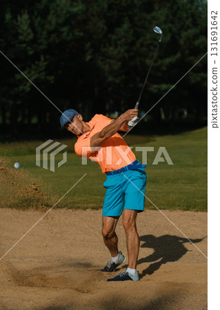 Golfer practicing swing technique in sand trap on sunny day at golf course surrounded by trees 131691642