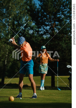 Golfers enjoying a sunny day on the course in vibrant attire during a casual afternoon game surrounded by lush trees 131691681