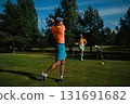 Golfer swings club on a sunny afternoon at a lush course while partner watches nearby with a playful demeanor and a colorful outfit 131691682