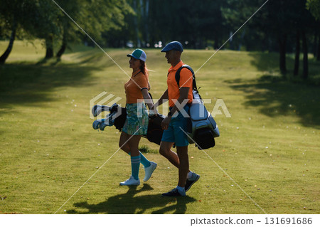 Couple walking together on a sunlit golf course carrying golf bags in vibrant attire during a warm afternoon 131691686