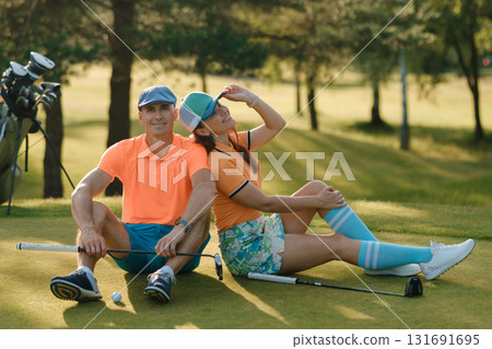 Couple enjoying a sunny day on the golf course while taking a break between rounds and sharing smiles with friends nearby 131691695